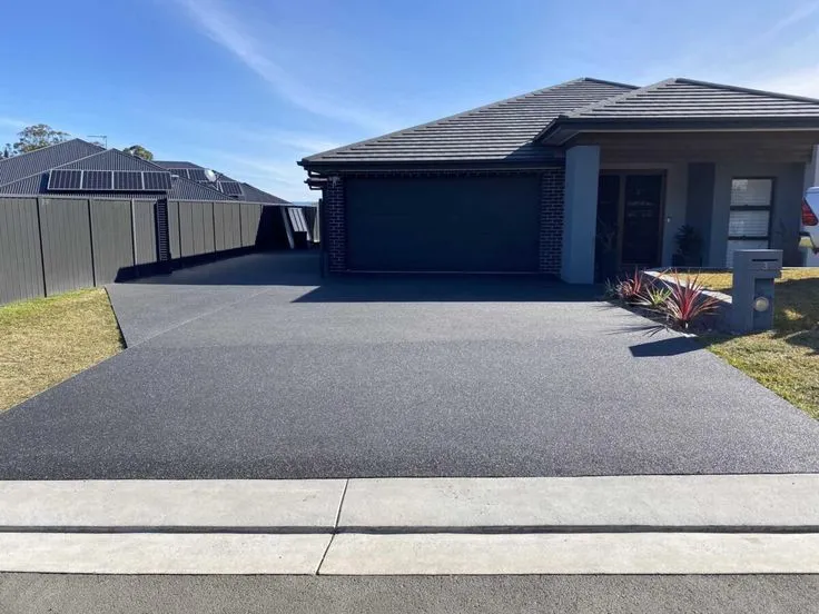 Modern residential driveway installation by concrete contractors in Dallas TX, featuring smooth charcoal-colored concrete with clean edges and solar panels visible.