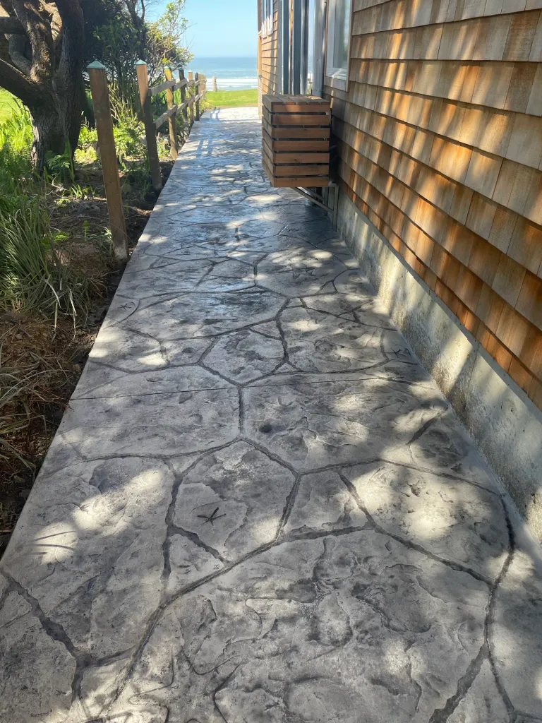 Seaside walkway with stamped concrete in Dallas TX showcasing natural slate texture and gray tones along coastal property.